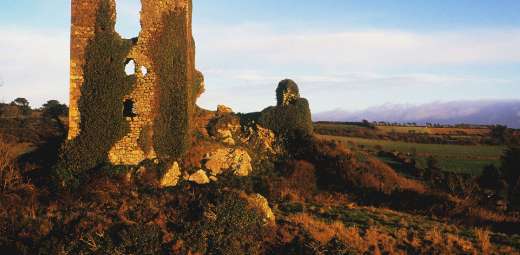 Ruins of an ancient stone structure, known as Dunhill Castle, standing solemnly in a field with a backdrop of a tranquil sky at dusk.