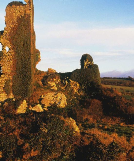 Ruins of Dunhill Castle, a historical landmark, amidst a rocky landscape under a clear sky at golden hour in Ireland.