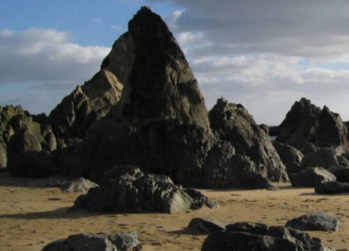 Rugged rocks emerge from the sandy Garrarus Strand beach against a backdrop of a cloudy sky in Ireland.