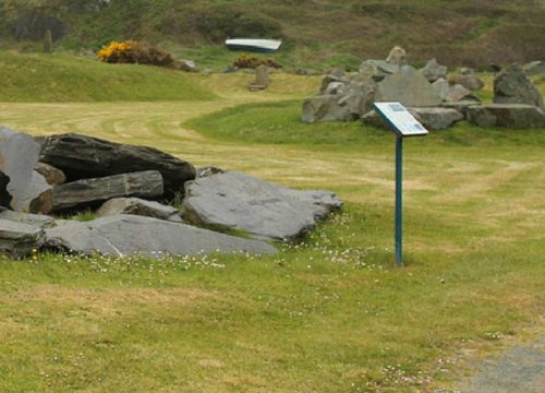 A tranquil outdoor setting in a Geological Garden with informational signposts amidst a landscape dotted with large rocks and patches of wildflowers, suggesting a place of natural interest or historical significance.