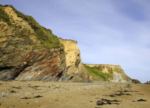 A serene Kilfarrasy Strand with rugged cliffs under a clear blue sky in Ireland.