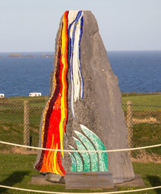 A vibrant mosaic artwork on a standing stone, with a background of calm blue seas and a clear sky, evokes the serenity of home.